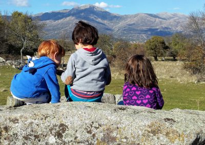 tres niñas del grupo de juego Aúlla, observan la montaña desde la Dehesa de Moralzarzal
